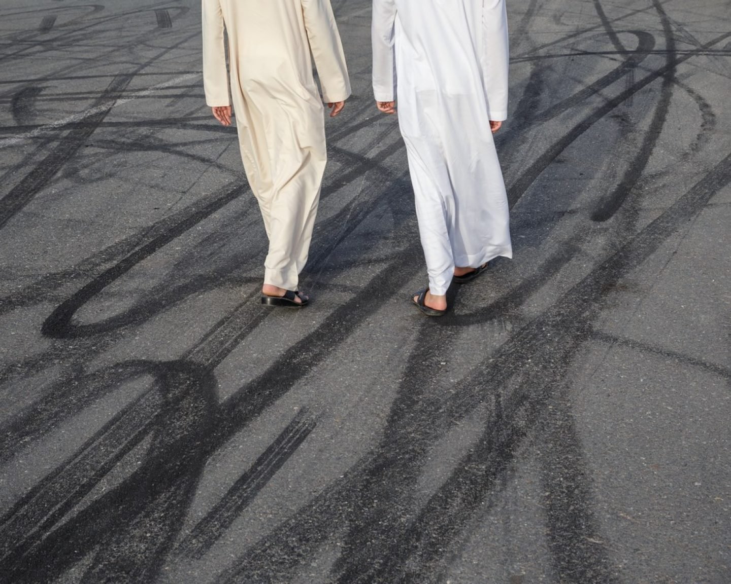 Two men cross a street marked by drifters' tires.