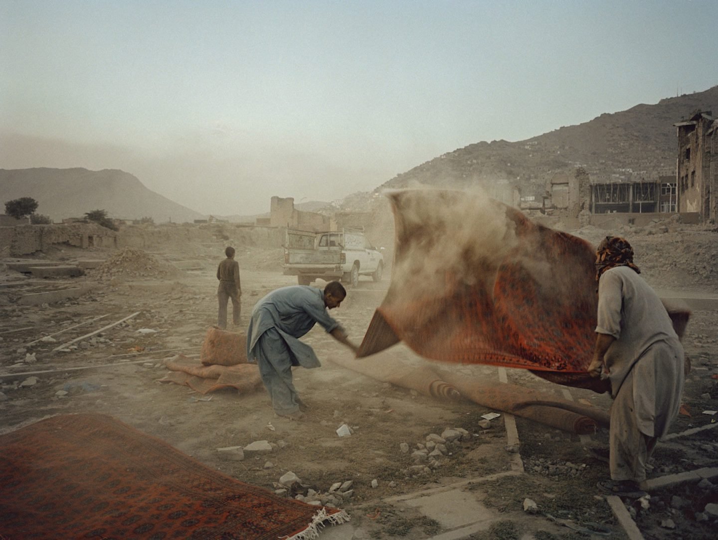AFGHANISTAN. Kabul. 2004. Men shake dust from rugs that were used for a wedding party.