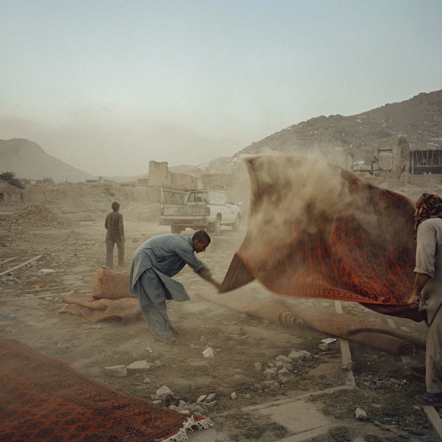 AFGHANISTAN. Kabul. 2004. Men shake dust from rugs that were used for a wedding party.